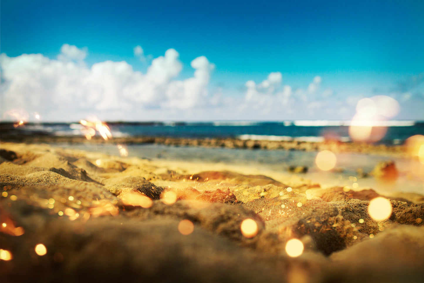 "Spark #1" is a fine art photograph that transports viewers to the serene shores of a beach in Hawaii. Shot at sand level, the image creates a unique perspective where only a small plane of focus is available, enveloping the scene with a dreamlike quality. The golden yellow sand stretches into the distance, contrasting beautifully against the deep blue sky. By Shannon Black